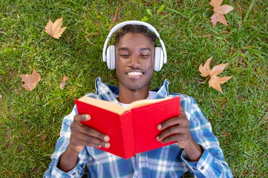 Contented black man on grass engrossed in book outside