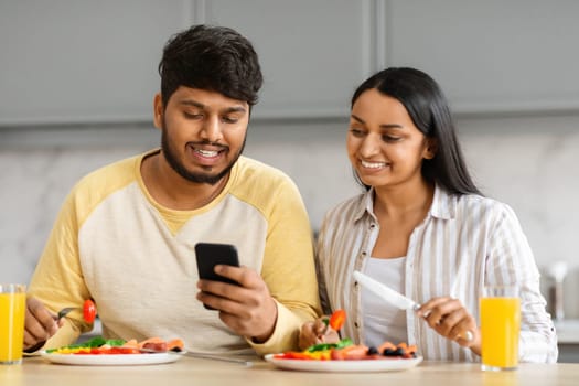 Millennial Indian Man And Woman Having Breakfast And Using Smartphone