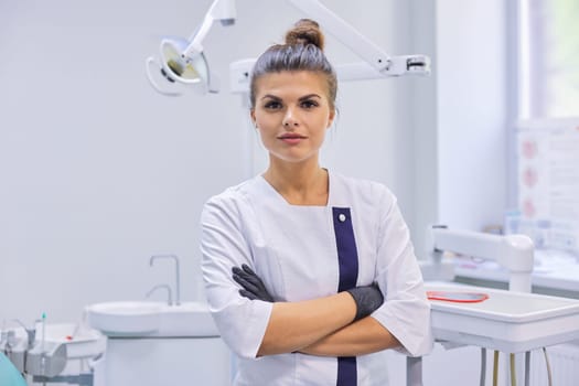 Portrait of young confident dentist doctor woman, female with arms crossed looking at camera standing in dentistry office