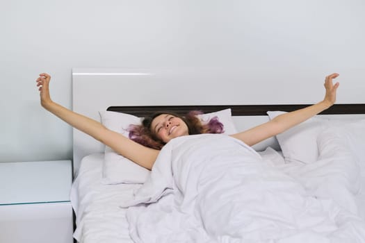 Teen girl waking up in the morning lying on pillow in bed with arms open