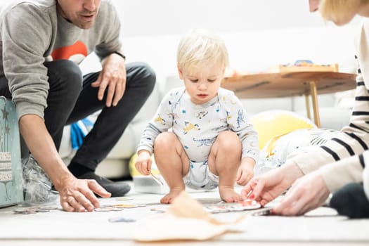 Parents playing games with child. Little toddler doing puzzle. Infant baby boy learns to solve problems and develops cognitive skills. Child development concept