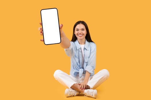 Smiling woman showing smartphone screen, sitting crossed-legged
