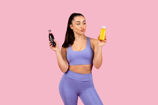 Fitness woman comparing drinks against pink background