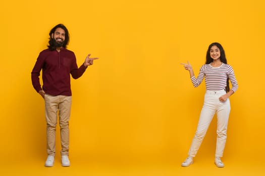 Cheerful young indian man and woman pointing at copy space