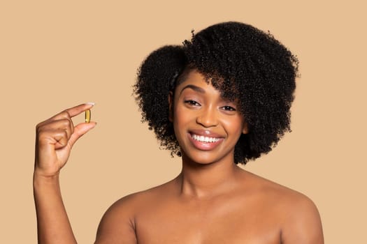 Happy black woman holding supplement, curly hair, beige backdrop