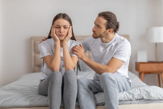 Man comforting distressed woman sitting on bed