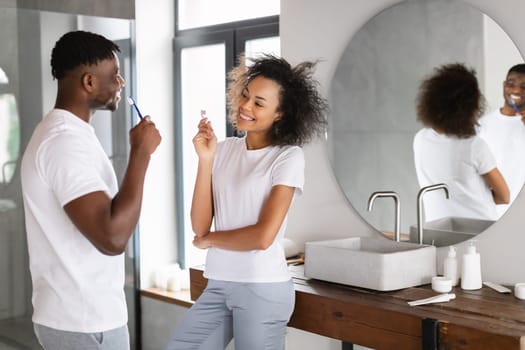 African American Couple Smiling While Brushing Teeth In Modern Bathroom