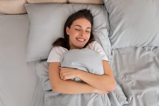 Happy woman hugging blanket, lying in bed, top view