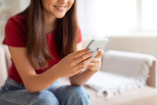 Young asian woman focused on her smartphone sitting on couch at home