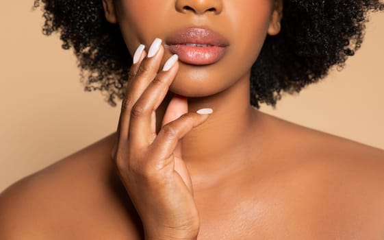Close-up of black woman's lips and chin, touching face, beige backdrop
