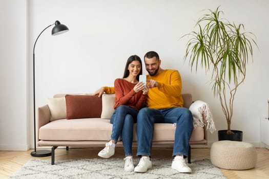 Beautiful Young Couple Using Mobile Phone While Relaxing On Couch At Home