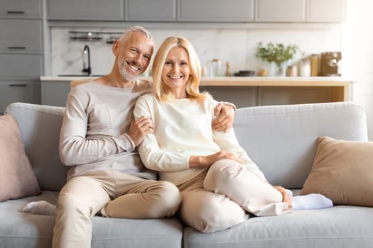 Happy loving senior spouses sitting on couch at home