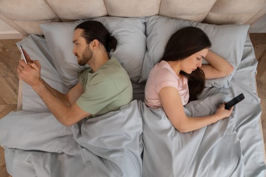 Couple in bed on phones, lying back to back