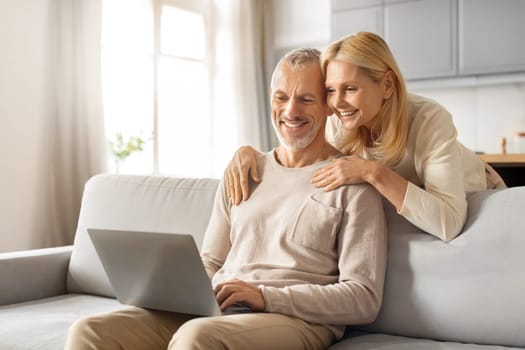 Positive beautiful loving senior spouses using laptop at home