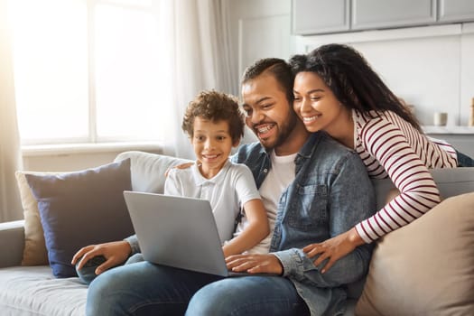 Happy young black family of three using laptop together at home