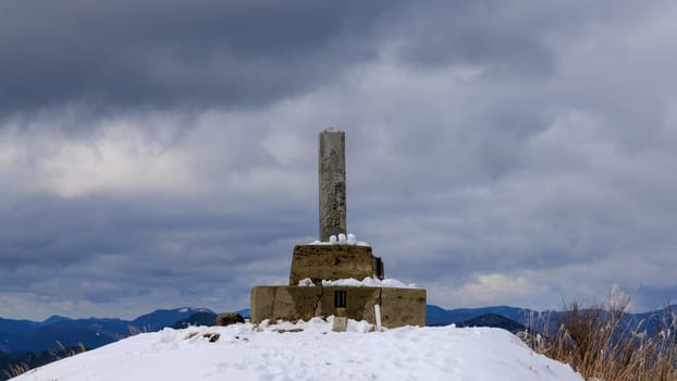 Stone concrete marker on summit of snowy mountain on cloudy day
