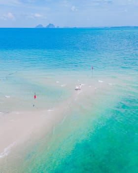 a couple of men and woman walking at a sandbar in the ocean of Koh Muk, a tropical island with palm trees and soft white sand, and a turqouse colored ocean in Koh Mook Trang Thailand