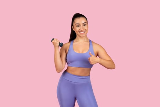 Smiling woman giving thumbs up while lifting dumbbell
