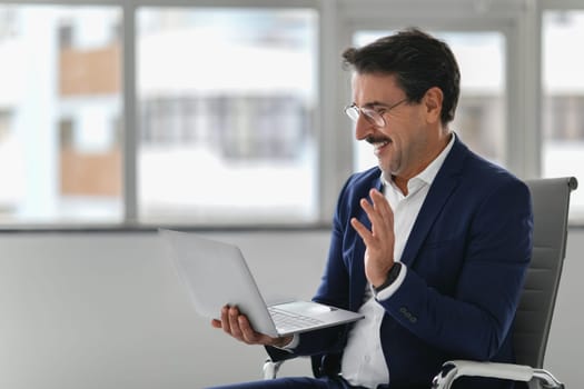 Joyful businessman in a blue suit laughing and gesturing during a video call on his laptop