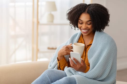 A woman wrapped in a cozy blue blanket smiles while holding a white mug in one hand