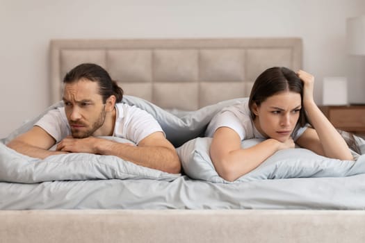 Couple in bed with worried expressions facing away