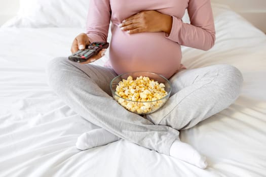 Cropped Shot Of Pregnant Woman With Popcorn And Remote Controller In Hands