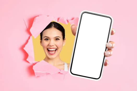 Joyful lady presenting cell phone breaking through pink backdrop