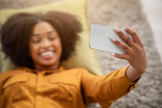 Smiling African American woman with curly hair takes a selfie while lying down
