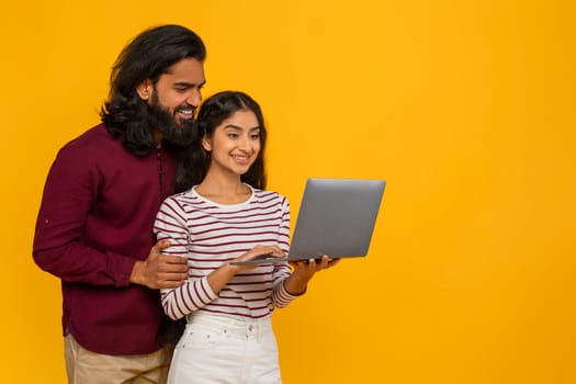 Happy indian couple with laptop on yellow background