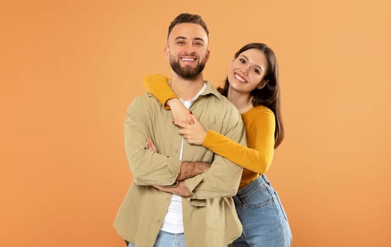 Smiling European Young Couple Hugging Over Orange Studio Background
