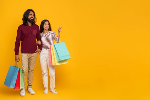 Cheerful millennial indian couple shopping together on yellow