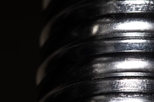 Close up of the thread of a metallic screw on black