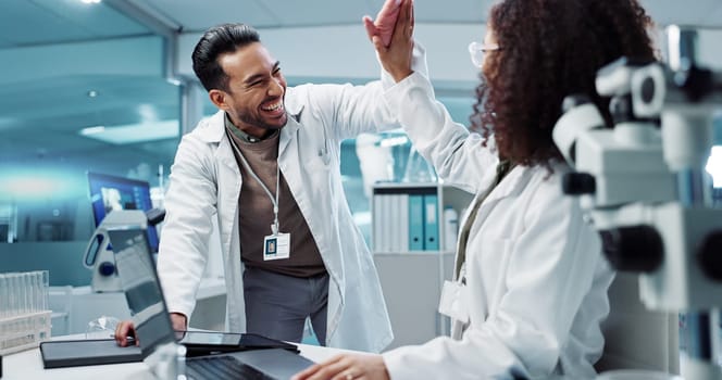 Scientist, teamwork and high five with laptop in laboratory for test breakthrough, pharmaceutical review or success. Science, collaboration or technology for research, discussion and digital analysis