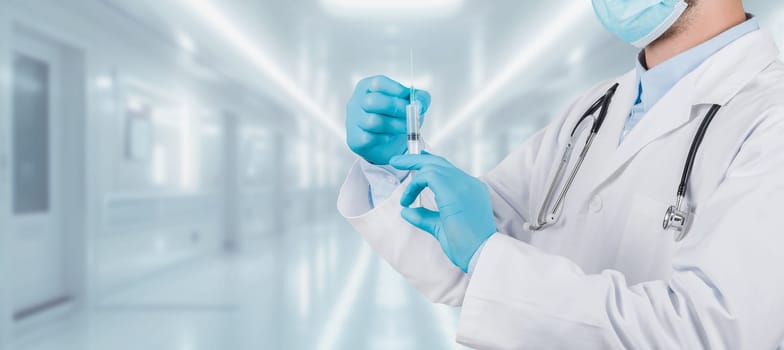 A healthcare professional in a white lab coat and surgical mask prepares a vaccine in a syringe