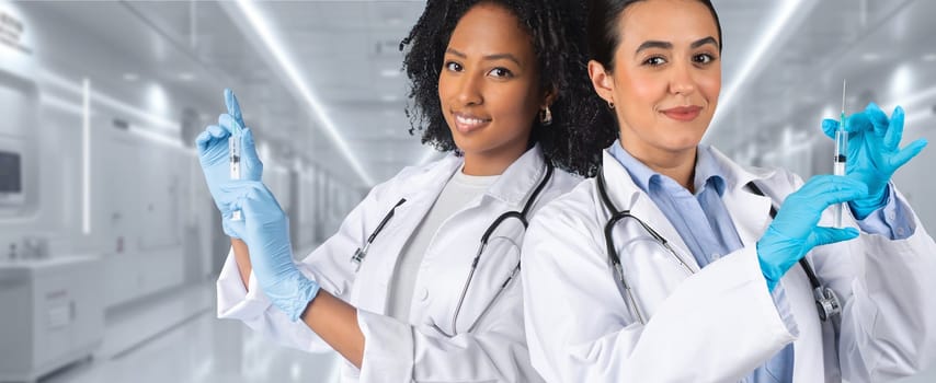 Two women medical professionals in white lab coats and blue gloves holding syringes