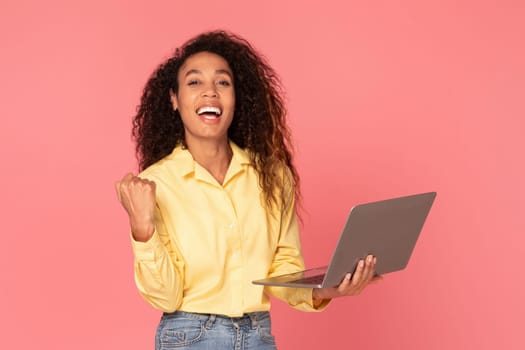 Victorious black woman with laptop in yellow shirt