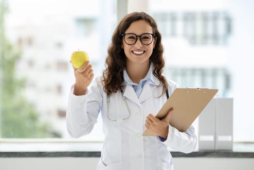 Friendly young woman doctor general physician showing apple
