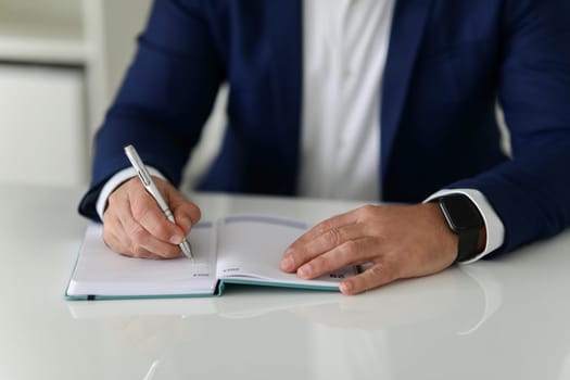 Close-up of a businessman hands writing in a notebook, wearing a smartwatch and a blue suit