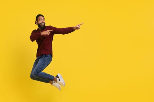 Emotional excited millennial indian guy jumping, showing advertisement