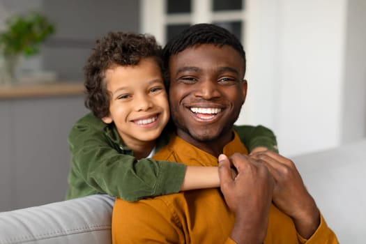 Cheerful black son hugs father from behind with bright smiles