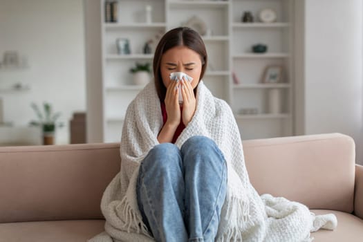 Young asian woman feeling unwell at home, sneezing into tissue