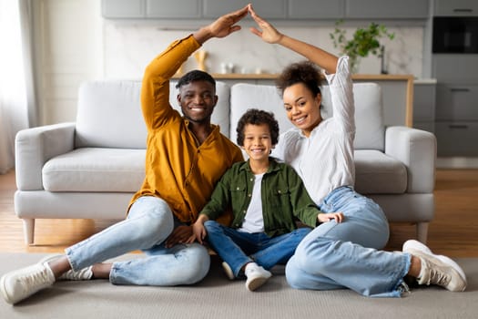 Joyful black family making house shape with hands at home