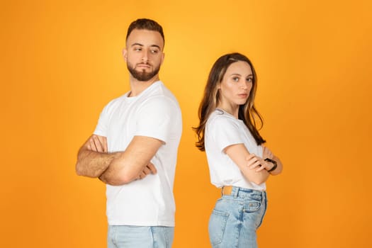 A man and woman in white shirts and denim jeans stand back to back with arms crossed