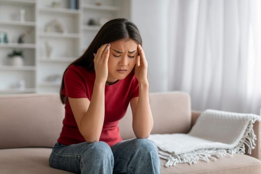 Stressed young asian woman suffering from severe headache or migraine at home