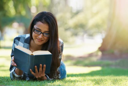 Happy woman, student and reading at park with book for literature, studying or story in nature. Female person, smart or young adult with smile or glasses for chapter, learning or outdoor education