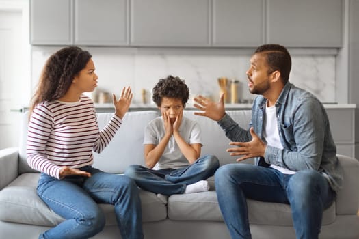 Upset black boy sitting with hands on cheeks while his parents argue