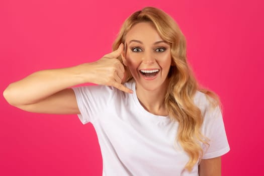 Cheerful millennial blonde lady gesturing Call Me on pink background