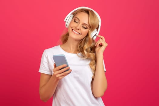 Happy blonde woman with smartphone and headphones listening music, studio