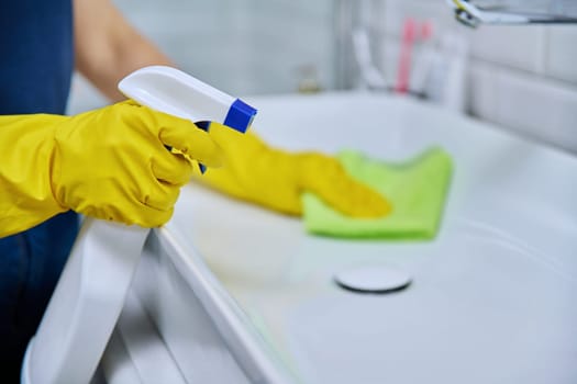 Close-up of cleaning sink with faucet in bathroom, hands in gloves with detergent