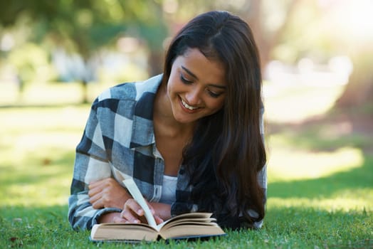Woman, information and reading book on grass, literature and smiling for fiction or fantasy story. Female person, nature and relaxing on lawn for knowledge, novel and student studying in garden